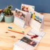 Calendario personalizado con fotos tamaño sobremsa 21x15 de Fotoprix. Foto en uso del calendario pasando página del mes colocado en una mesa.