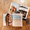 Álbumes de Fotoprix. Foto de dos Fotolibros abiertos con foto a doble página y texto explicativo, colocados en una mesa de casa a modo decorativo.