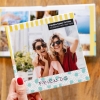 Álbumes de Fotoprix. Foto de uso de un Fotolibro square 21x27 sujetándolo con la mano y otro completamente abierto colocado en una mesa del hogar.