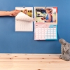 Calendario personalizado con fotos tamaño mediano A3 de Fotoprix. Foto en uso del calendario pasando página del mes mientras está colgado en la pared.
