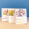 Productos Fotoprix, tres calendarios personalizados con fotos de tamaño 14x15 sobremesa de Fotoprix decorando una mesita de madera.