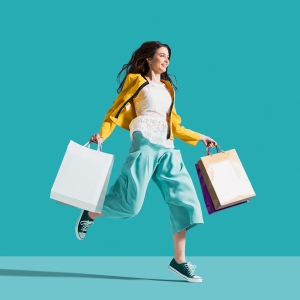 Disfruta la alegría de hacer tus compras cerca de casa. Chica joven camina feliz a saltitos con sus bolsas de la compra que ha realizado cerca de su hogar.