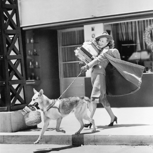 Foto retro de una mujer paseando a su perro y llena de bolsas de la compra, hace referencia a que en cualquier sitio en el que se esté, hay una tienda Fotoprix.
