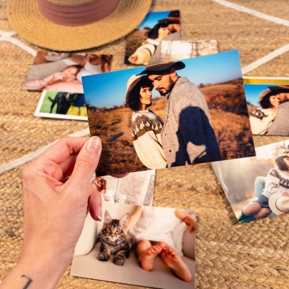 Tamaño de impresión Fotoprix, copias de 10x15. Tamaño de impresión de Fotoprix, foto en uso de varias copias de tamaño 10x15 y sujetando una de ellas mientras el resto están en una mesa.
