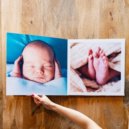 Tamaños de Álbumes Fotoprix, foto sujetando uno de 35x35. Tamaños de Álbumes Fotoprix. Foto en uso sujetando uno de 35x35 abierto totalmente y colocado decorando una mesita de madera.