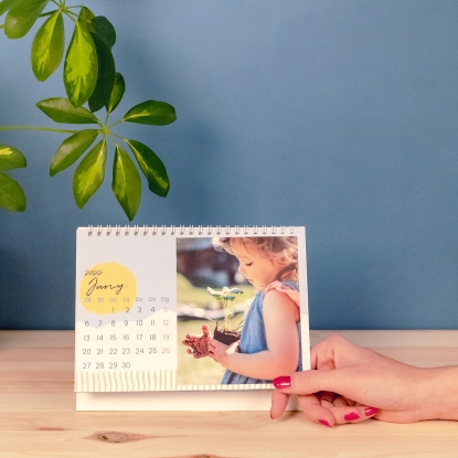 Calendario personalizado de sobremesa Fotoprix, tamaño 21x15. Calendario personalizads con fotos de tamaño 21x15 sobremesa de Fotoprix. Foto de un calendario abierto en el mes de Junio decorando mesa de madera.