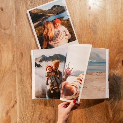 Productos de Fotoprix, foto en uso pasando una hoja de un Álbum Fotolibro clásico mientras está colocado en una mesa junto a otro cerrado.