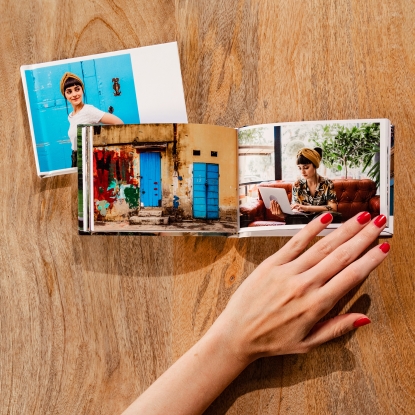 Tamaños de Álbumes Fotoprix, foto sujetando uno de 10x15. Tamaños de Álbumes Fotoprix. Foto en uso sujetando con la mano uno de 10x15 abierto totalmente y otro cerrado colocados decorando una mesita.