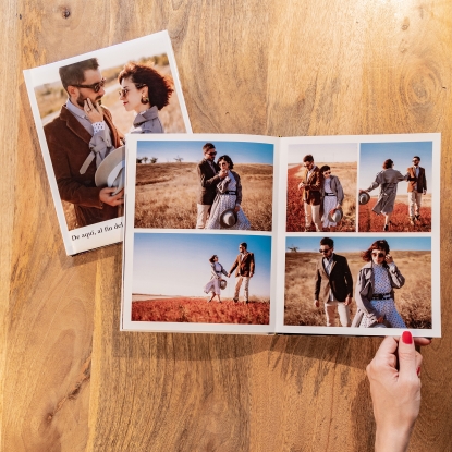 Productos de Fotoprix, foto en uso mano sujetando Álbum Fotolibro Plus abierto completamente y colocado en una mesa junto a otro cerrado.