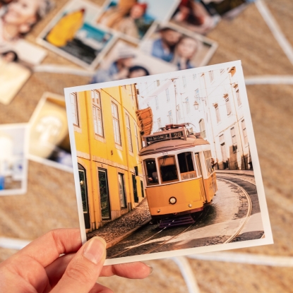 Tamaño de impresión Fotoprix, copias de 13x13. Tamaño de impresión de Fotoprix, foto en uso de varias copias de tamaño 13x13 y sujetando una de ellas mientras el resto están en una mesa.