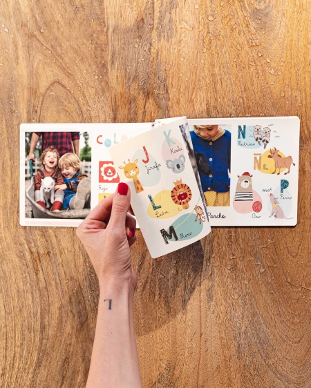 Álbumes de Fotoprix. Foto en uso de un Indestructible 21x27 pasándose una página del álbum mientras está colocado en una mesa del hogar.