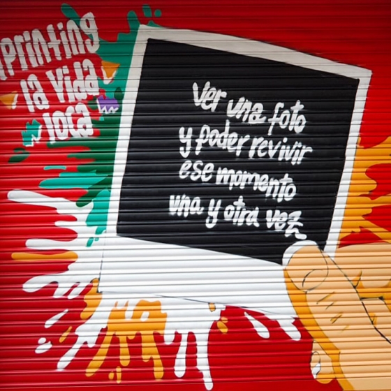 Imagen de la persiana de la tienda de fotografía franquiciada de Fotoprix en Hospitalet de Llobregat.
Donde aparece dibujada una foto impresa con el lema "ver una foto y poder revivir ese momento una y otra vez" junto con el slogan de la empresa "¡Printing la vida loca!".