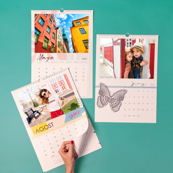Categoría de Fotoprix, calendarios de pared personalizados con fotos. Foto en uso pasando una de las páginas del mes mientras hay varios en una mesa.