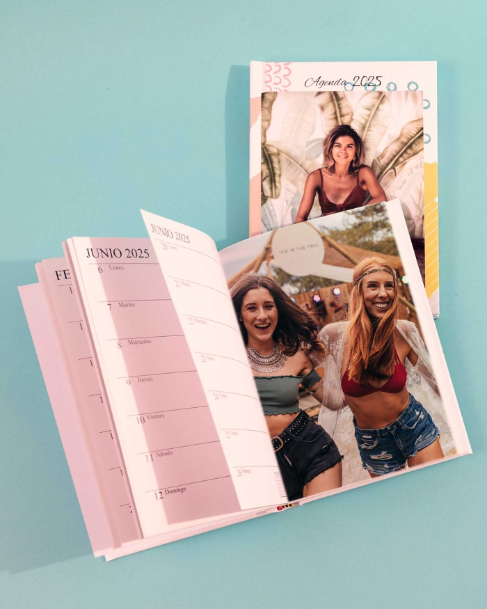 Imprenta de Fotoprix, agenda de tapa blanda abierta en el mes de Julio con una foto en la otra página y otra agenda cerrada en una superficie azul.
