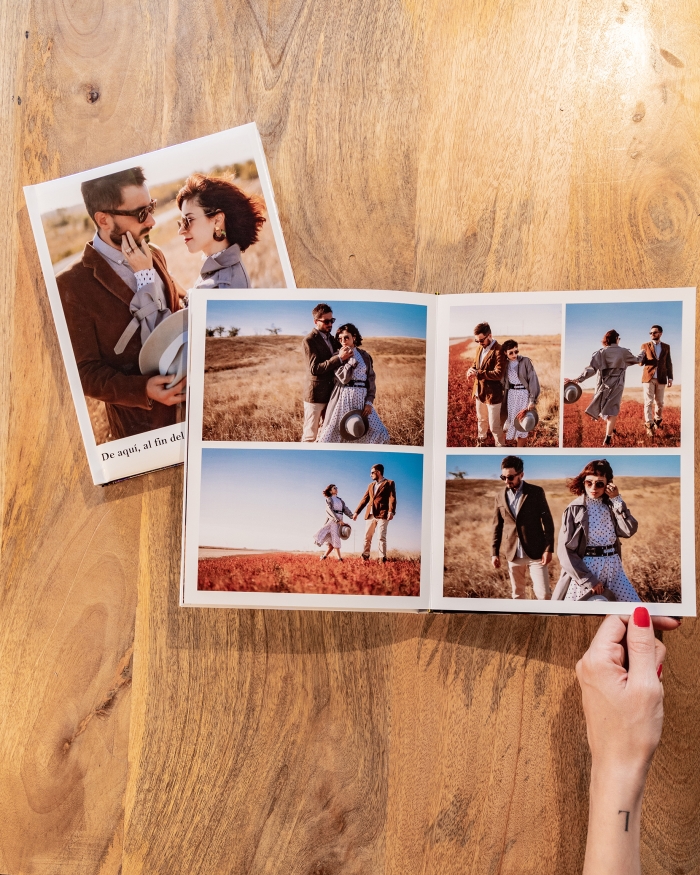 Productos de Fotoprix, foto en uso mano sujetando Álbum Fotolibro Plus abierto completamente y colocado en una mesa junto a otro cerrado.