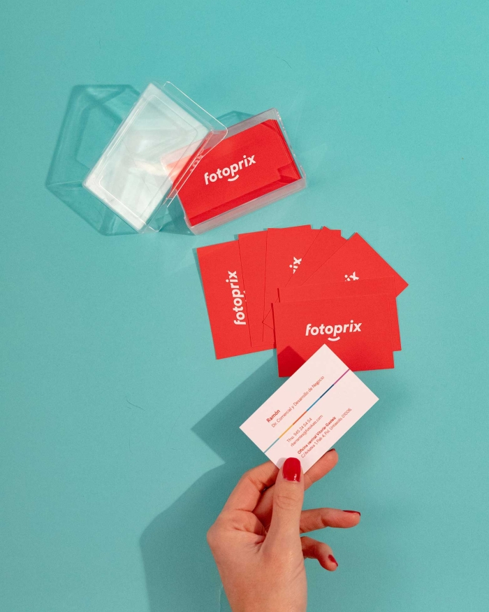 Imprenta de Fotoprix, foto en uso de una mano sujetando una tarjeta de visita de la empresa mientras hay otras colocadas en una superficie azul.