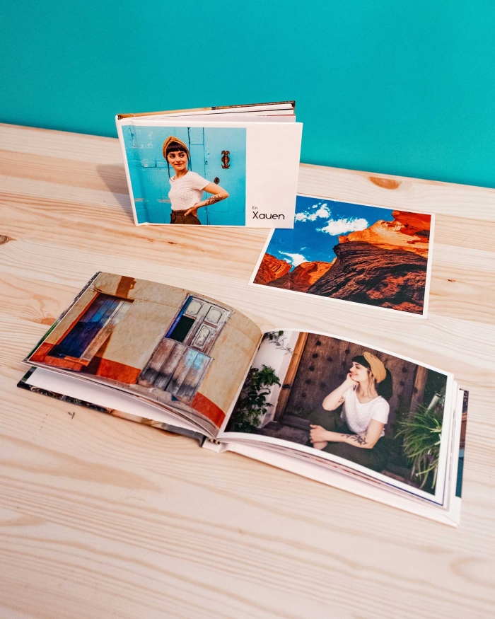Imagen en la que podemos ver dos pequeños álbumes 10x15. Uno abierto mostrando sus páginas a todo color y otro cerrado  de pie mostrando la portada personalizada junto a una fotografía impresa.