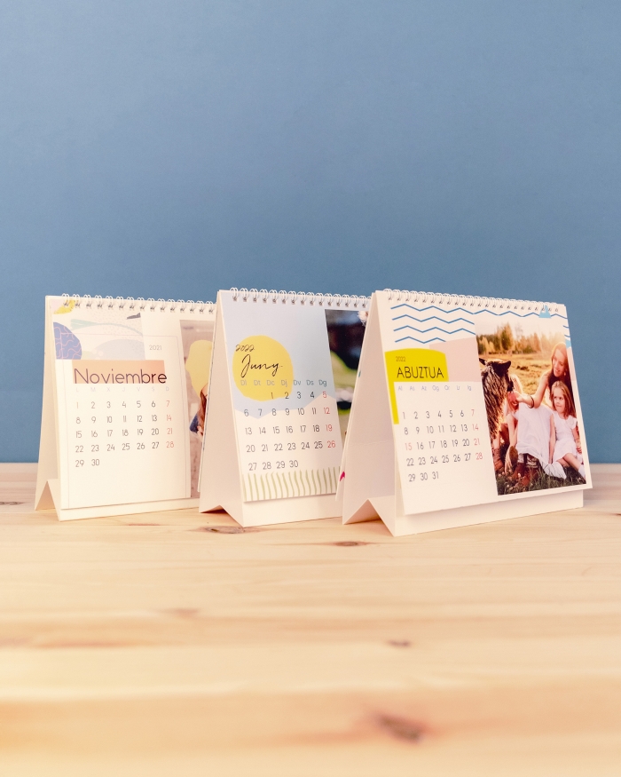 Productos Fotoprix, tres calendarios personalizados con fotos de tamaño 21x15 sobremesa de Fotoprix decorando una mesita de madera.