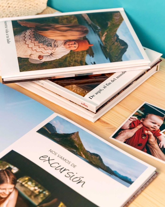 Álbumes de Fotoprix: Foto de varios Fotolibro Plus 21x27 colocados en una mesa de hogar, apreciándose las fotos y los textos de la portada y el grosor.