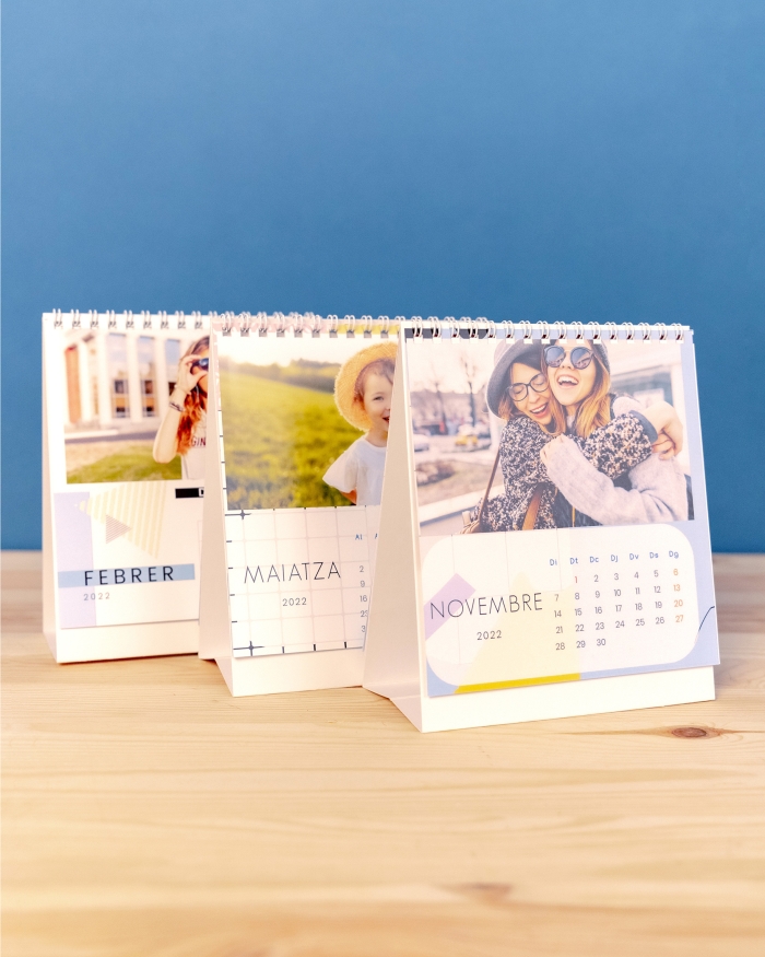 Productos Fotoprix, tres calendarios personalizados con fotos de tamaño 14x15 sobremesa de Fotoprix decorando una mesita de madera.